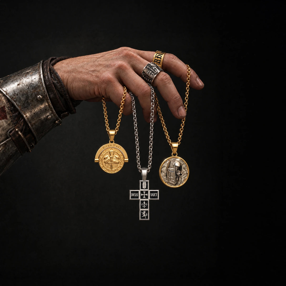 A gauntleted hand holding Deus Vult and Templar Skull pendants, wearing Crusades rings
